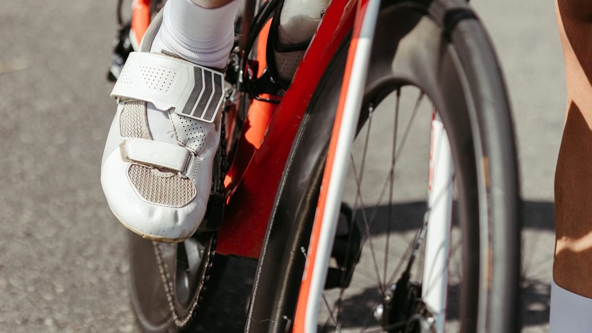 Chaussure de vélo de route blanche clipsée sur une pédale automatique, roue carbone en arrière-plan