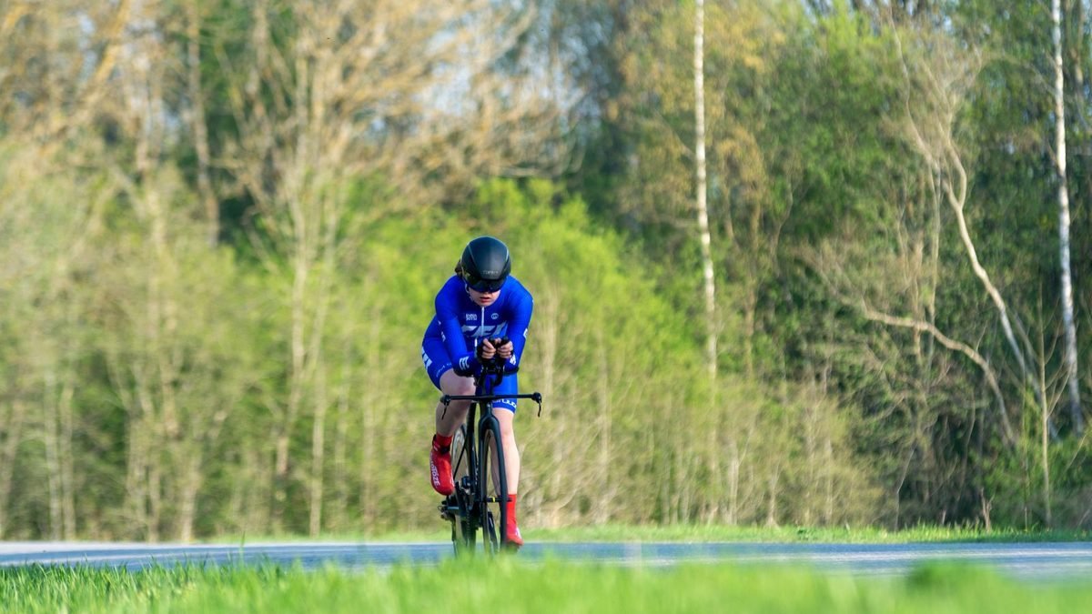 Cycliste en position aérodynamique avec casque profilé et combinaison sur une route de campagne