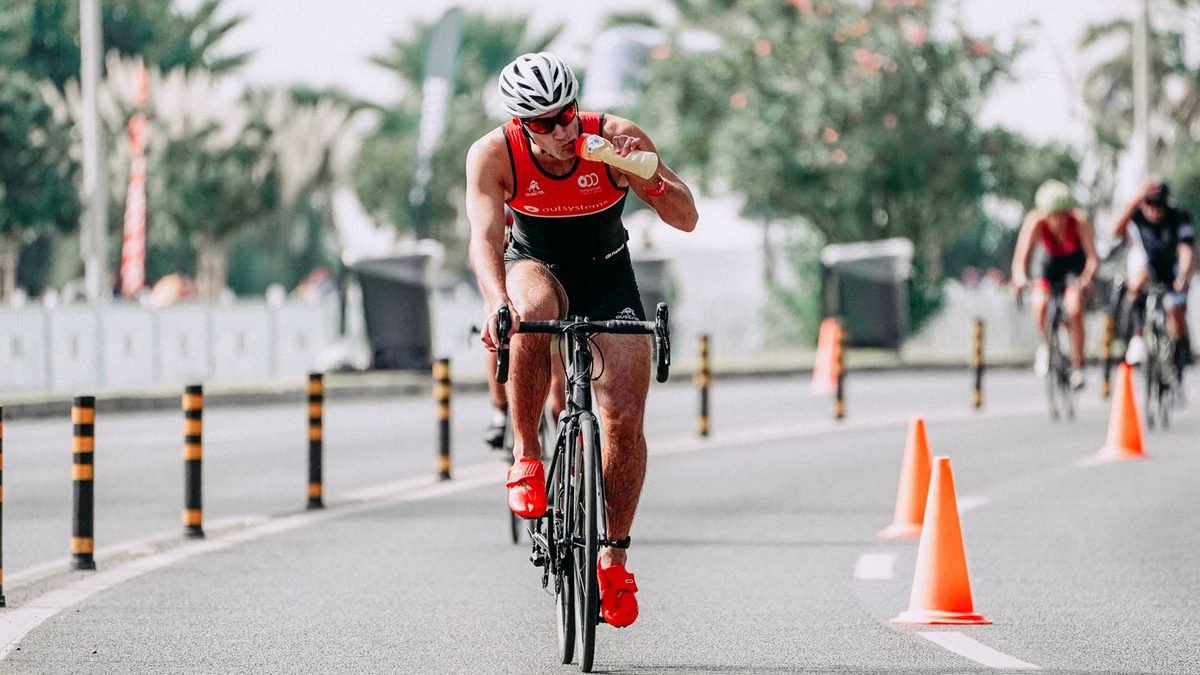 Cycliste sur un vélo de route qui boit à son bidon en pleine course, sans quitter la route des yeux