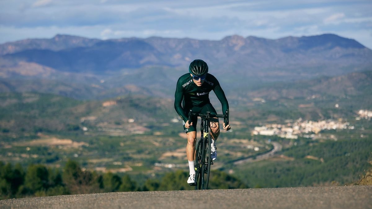 Cycliste en danseuse dans une montée de col, vallée et montagnes en arrière-plan